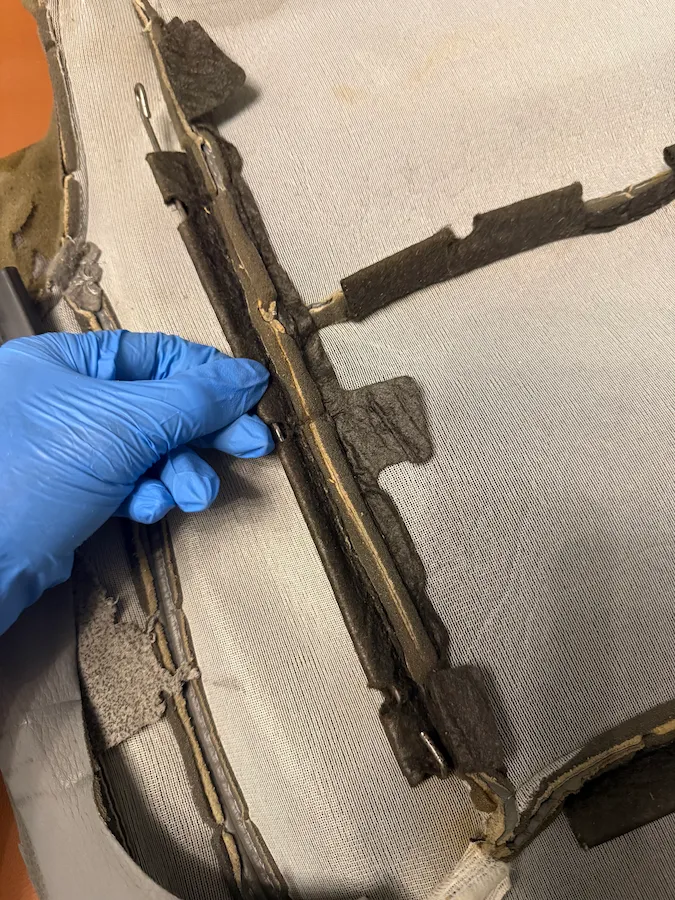 Technician reinforcing a separated leather seat seam from the underside before restitching